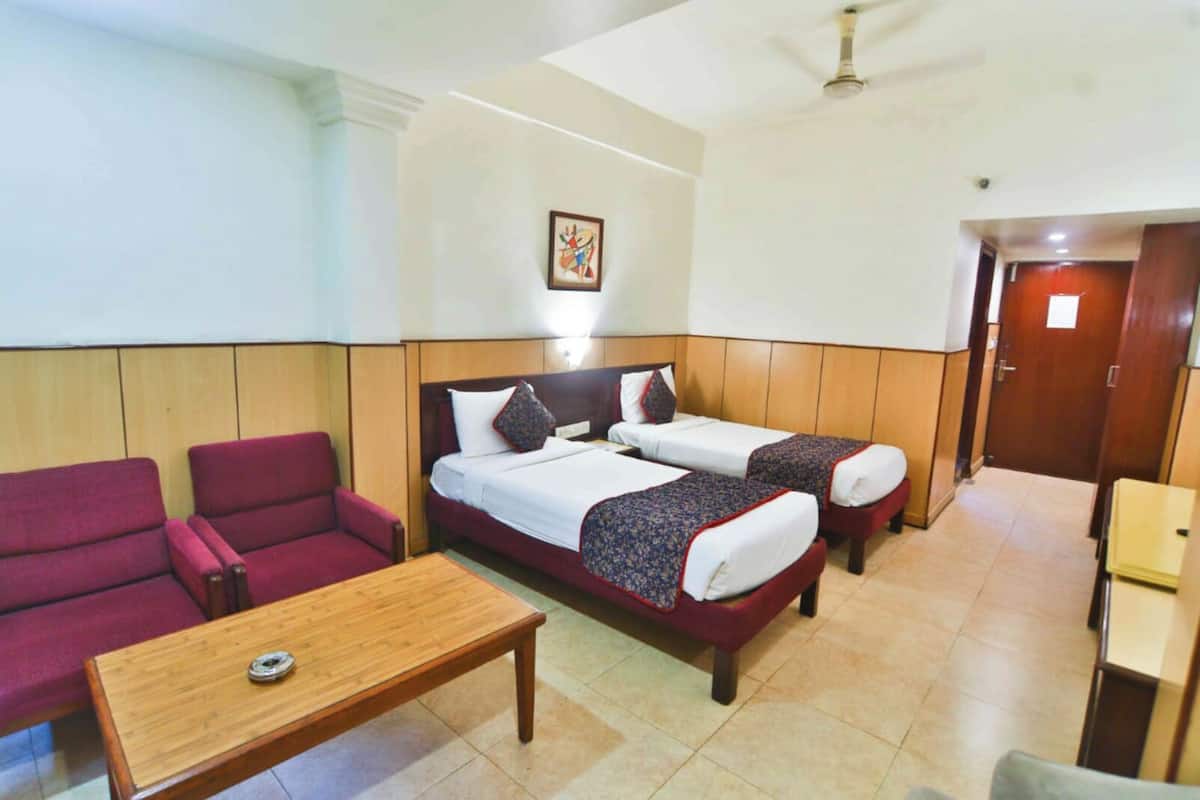 A hotel room with two beds, a red sofa, a wooden table, and a ceiling fan.