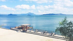 Une zone côtière avec une jetée s’avançant dans des eaux calmes, une petite construction dotée d’un toit, et des montagnes lointaines sous un ciel dégagé.