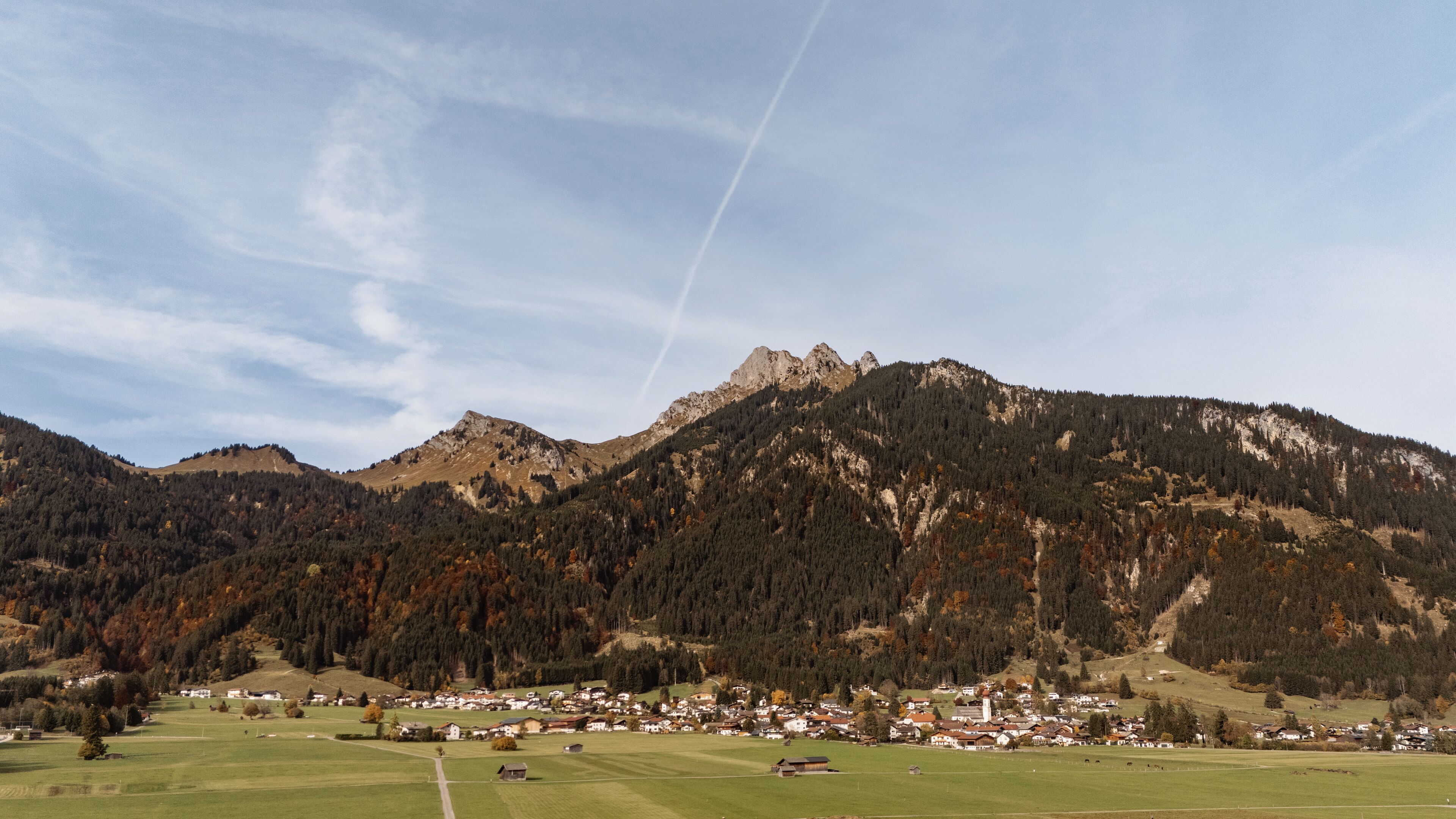 A mountain town with a prominent mountain range in the background, a small village with houses and a church, and a clear sky.