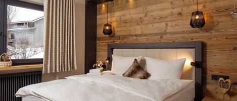 A bedroom with a wooden headboard, a bed with white linens, a window with curtains, and two wall-mounted lamps.