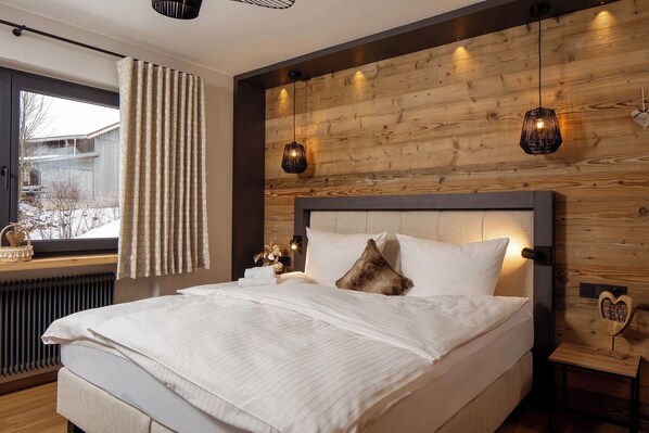 A bedroom with a wooden headboard, a bed with white linens, a window with curtains, and two wall-mounted lamps.