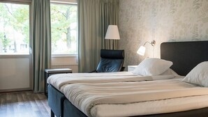 Een hotelkamer met een bed, een stoel, een lamp en een raam met gordijnen.