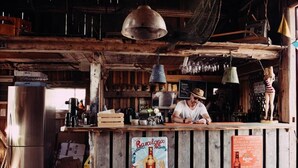Een rustieke bar met houten balken, een oude bierposter en een naambord.
