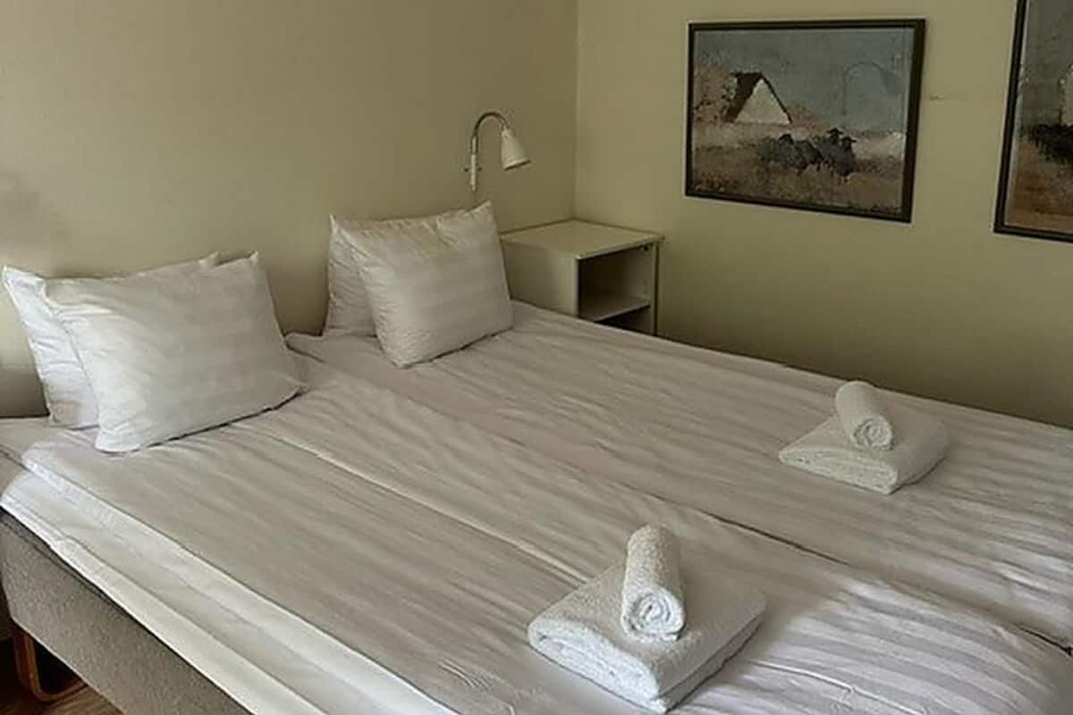 A hotel room with a bed, pillows, a nightstand, a lamp, and a painting on the wall.