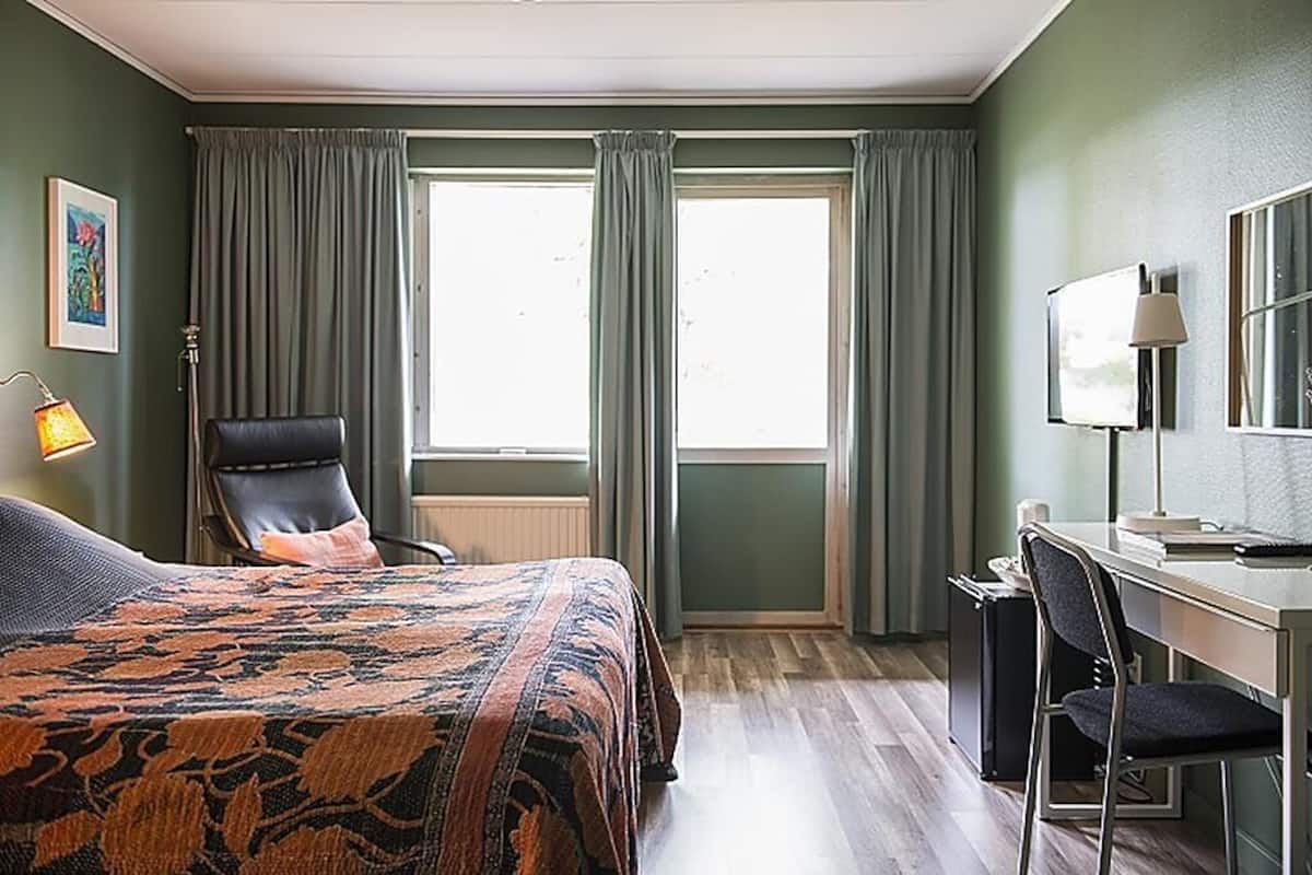 A hotel room with a bed, a desk, a chair, a lamp, and a window with curtains.