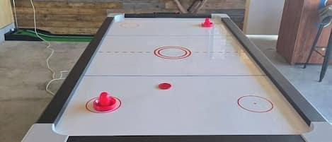 Een tafelvoetbaltafel met vier rode en één witte bal, voor een houten wand met een pokertafel op de achtergrond.