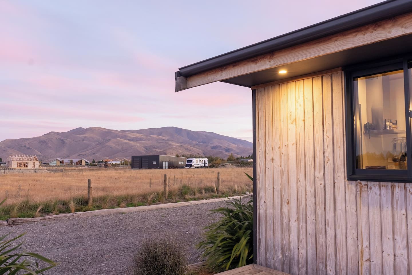 A modern building with a wooden exterior and a large window, set against a backdrop of mountains and a clear sky.