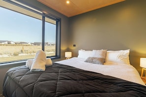 A bedroom with a large bed, a view of the outdoors, and a window. - The Games Room - Epic Views & Mancave Magic (Twizel)