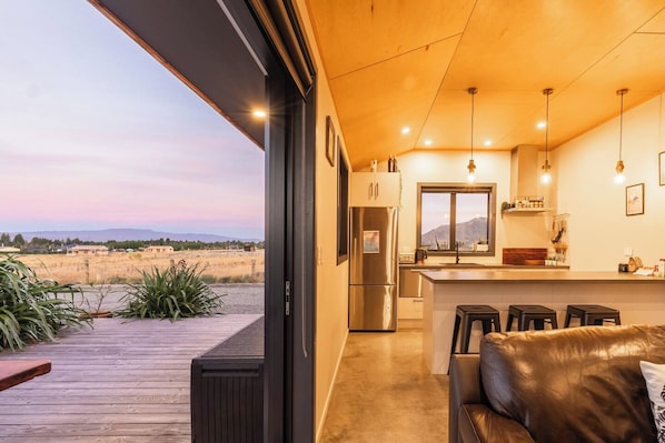 A modern kitchen with a large island, bar stools, and a view of the desert landscape. - The Games Room - Epic Views & Mancave Magic (Twizel)
