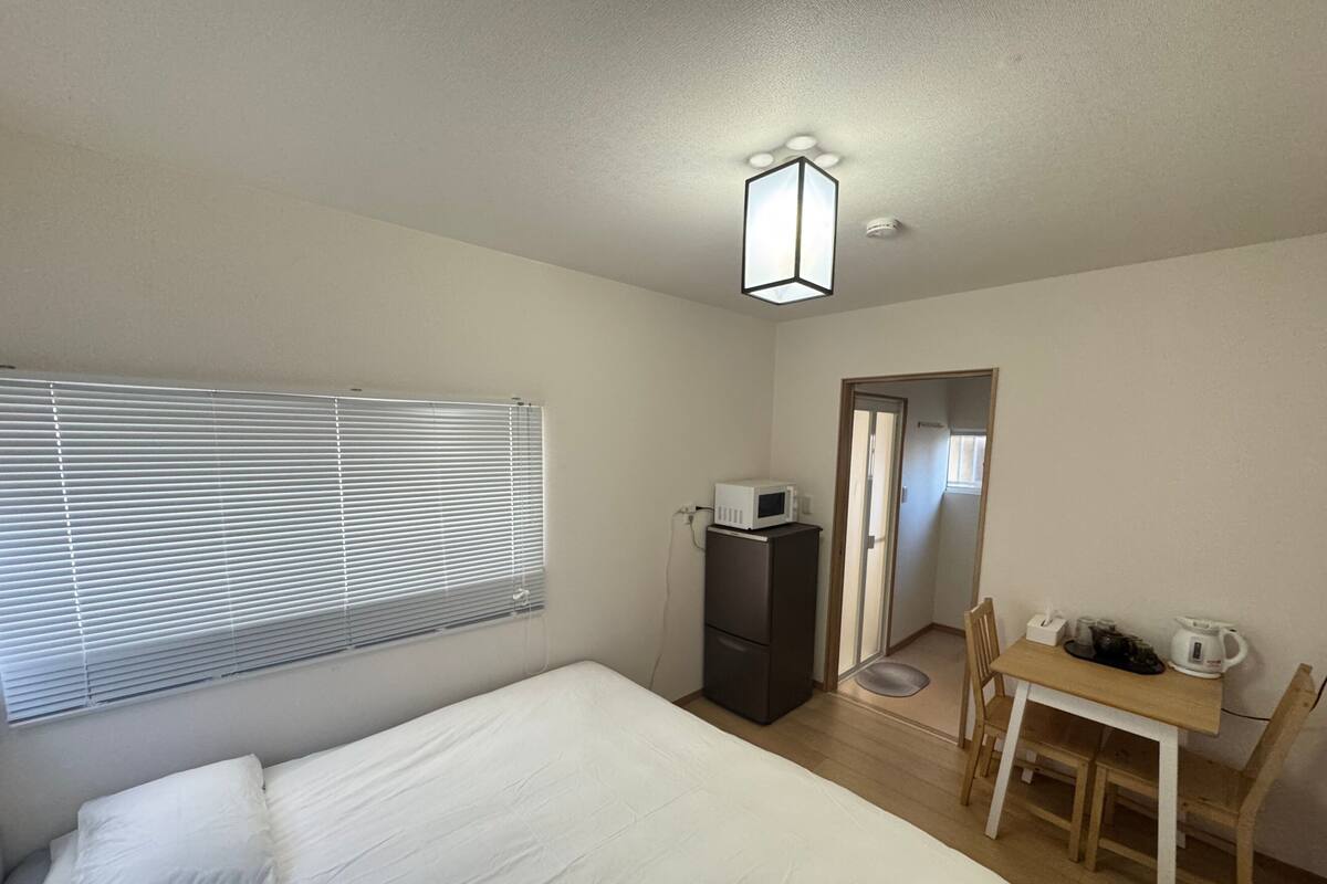 Un dormitorio con cama, escritorio con silla, microondas y una puerta que da a otra habitación.
