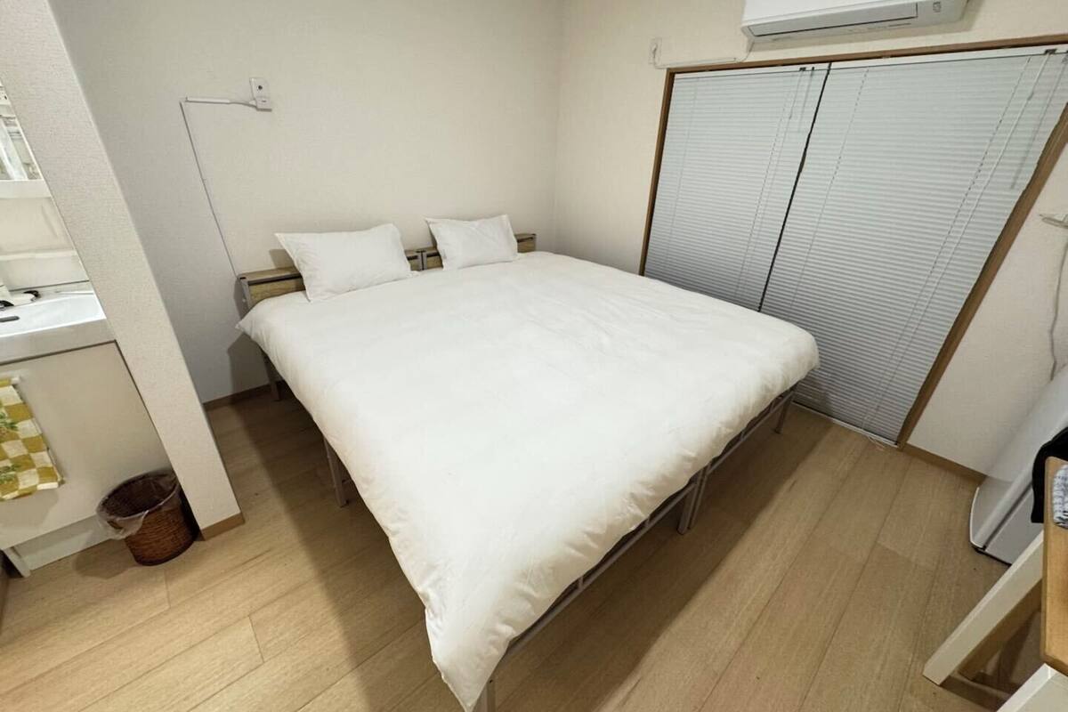 Habitación individual con ropa blanca de cama, una mesita de noche, una lámpara, un armario con puerta corredera y un equipo de aire acondicionado en la pared.