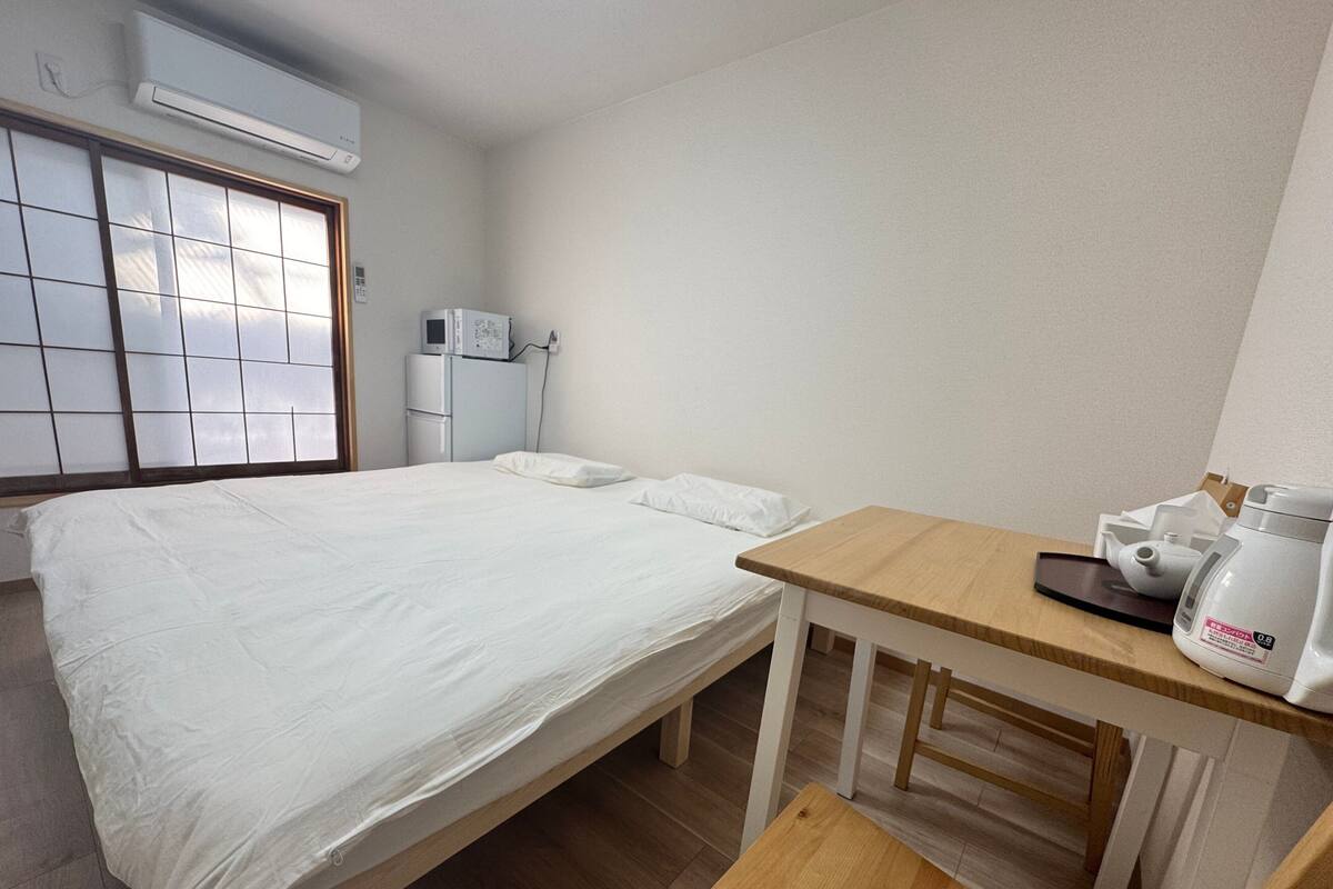 Una habitación de hotel con una cama, una mesita con hervidor, microondas y refrigerador.