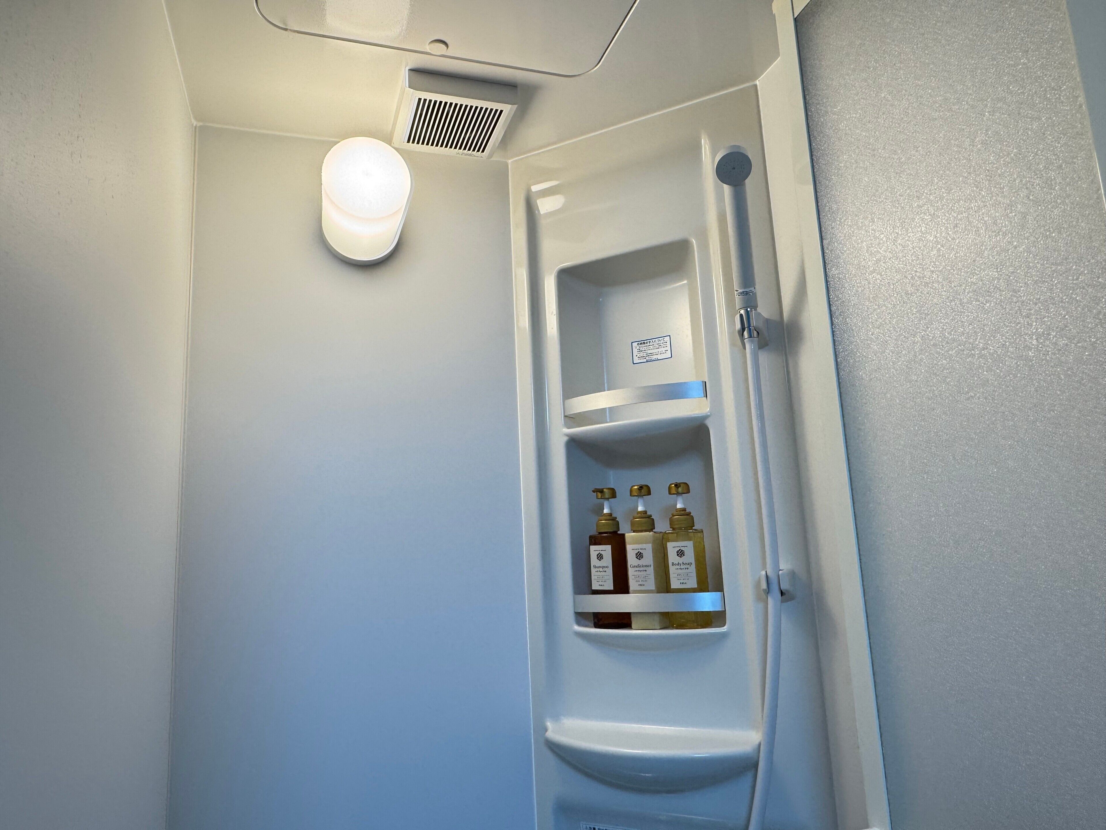 A bathroom with a white sink, a mirror, a shower, and a shelf with toiletries.