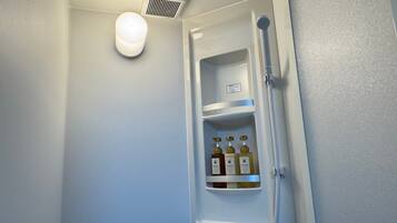 A bathroom with a white sink, a mirror, a shower, and a shelf with toiletries.