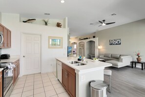 A modern kitchen with a central island, a dining area with a sofa, and a ceiling fan. - Four Bedrooms, 3 Baths, No Rear Neighbors,  Just Minutes walk  to Clubhouse (Kissimmee)