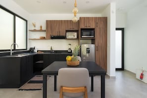 A modern kitchen with dark cabinetry, a black countertop, and a wooden dining table. - Bo Jungle - Steps to Tamarindo Beach - Surf & Pool #3 (Playa Langosta)
