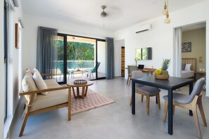 A modern living room with a sofa, dining table, and chairs. There is a balcony with a view of greenery. - Bo Jungle - Steps to Tamarindo Beach - Surf & Pool #4 (Playa Langosta)