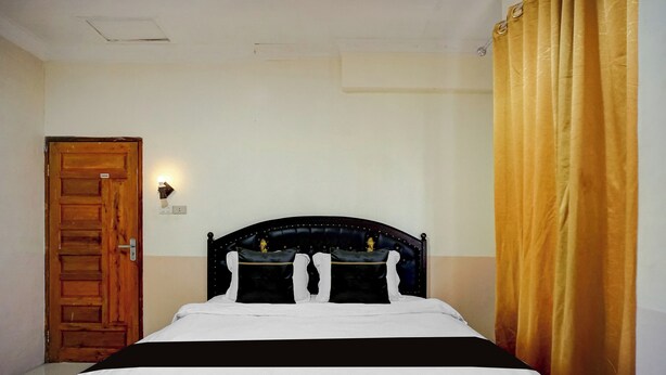 A bedroom with a wooden door, a bed with a dark headboard, and a curtain. - Hotel O near Monument Historique Berasta (Berastagi)