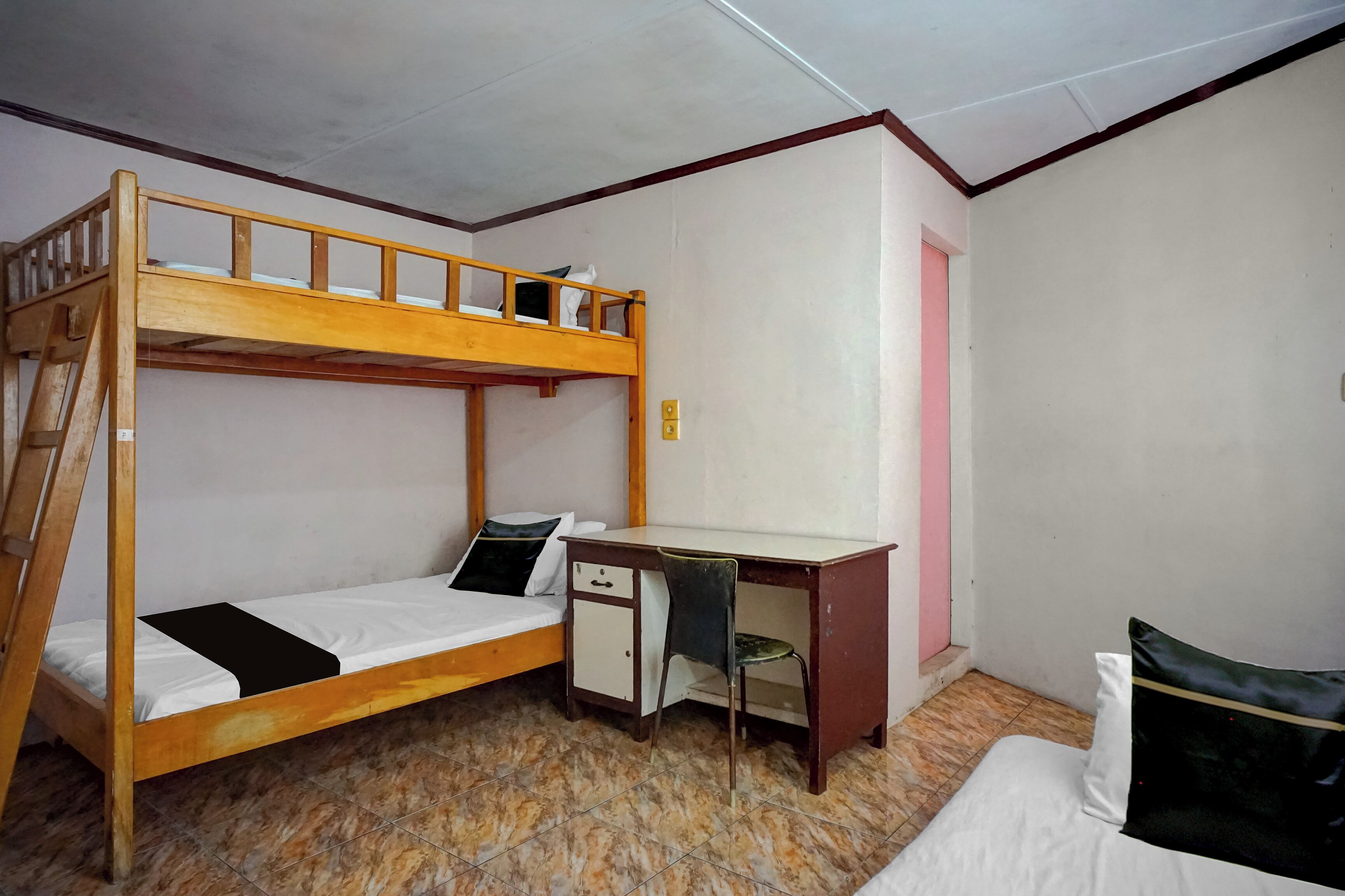 A bunk bed with a desk and chair, a small cabinet, and a pink door.