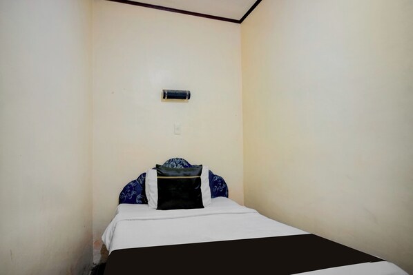 Una habitación pequeña con cama individual, pared sencilla, unidad de aire acondicionado y ropa de cama con estampado blanco y negro.