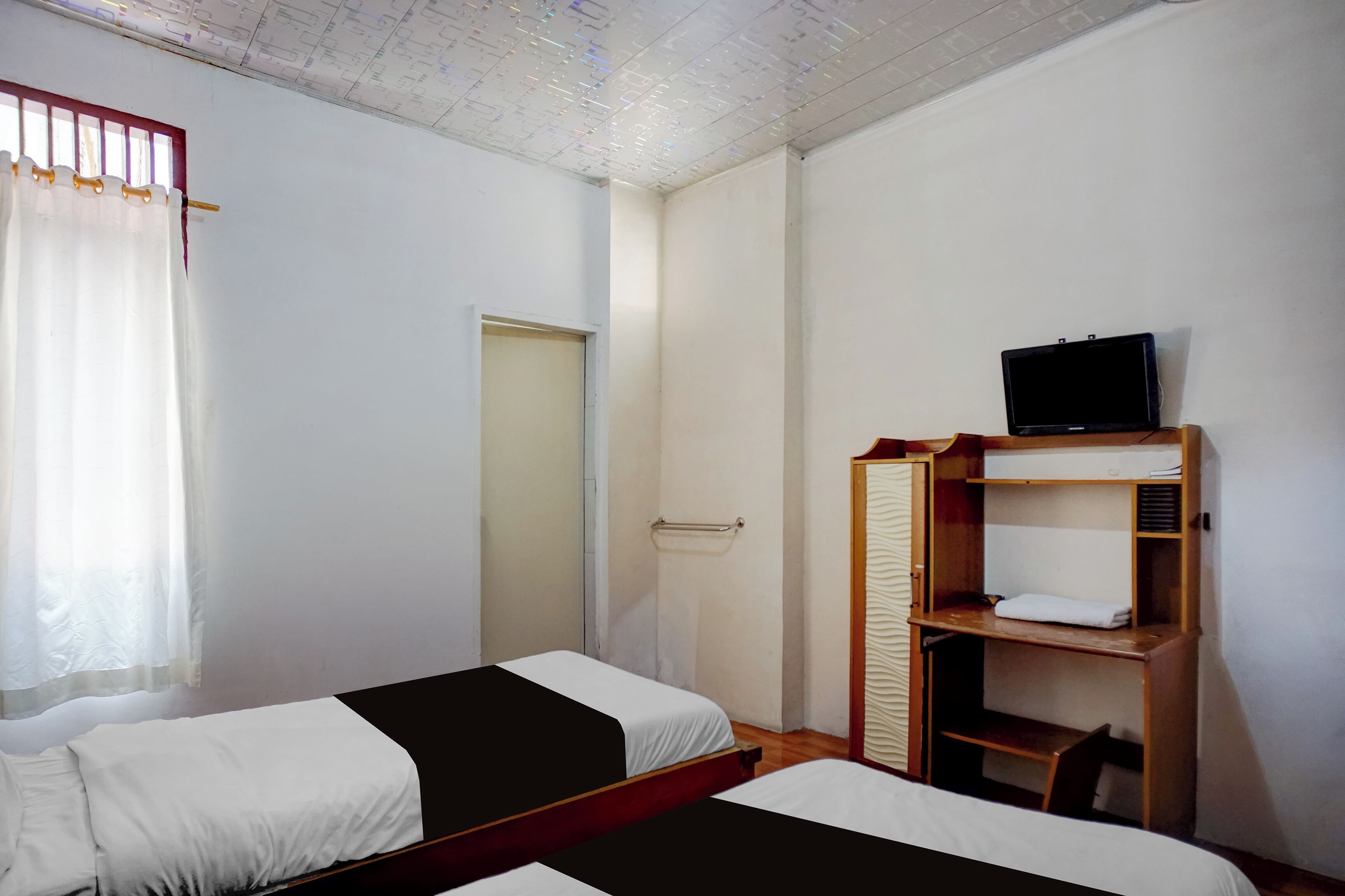 A room with two beds, a wooden wardrobe, a television, and a door.