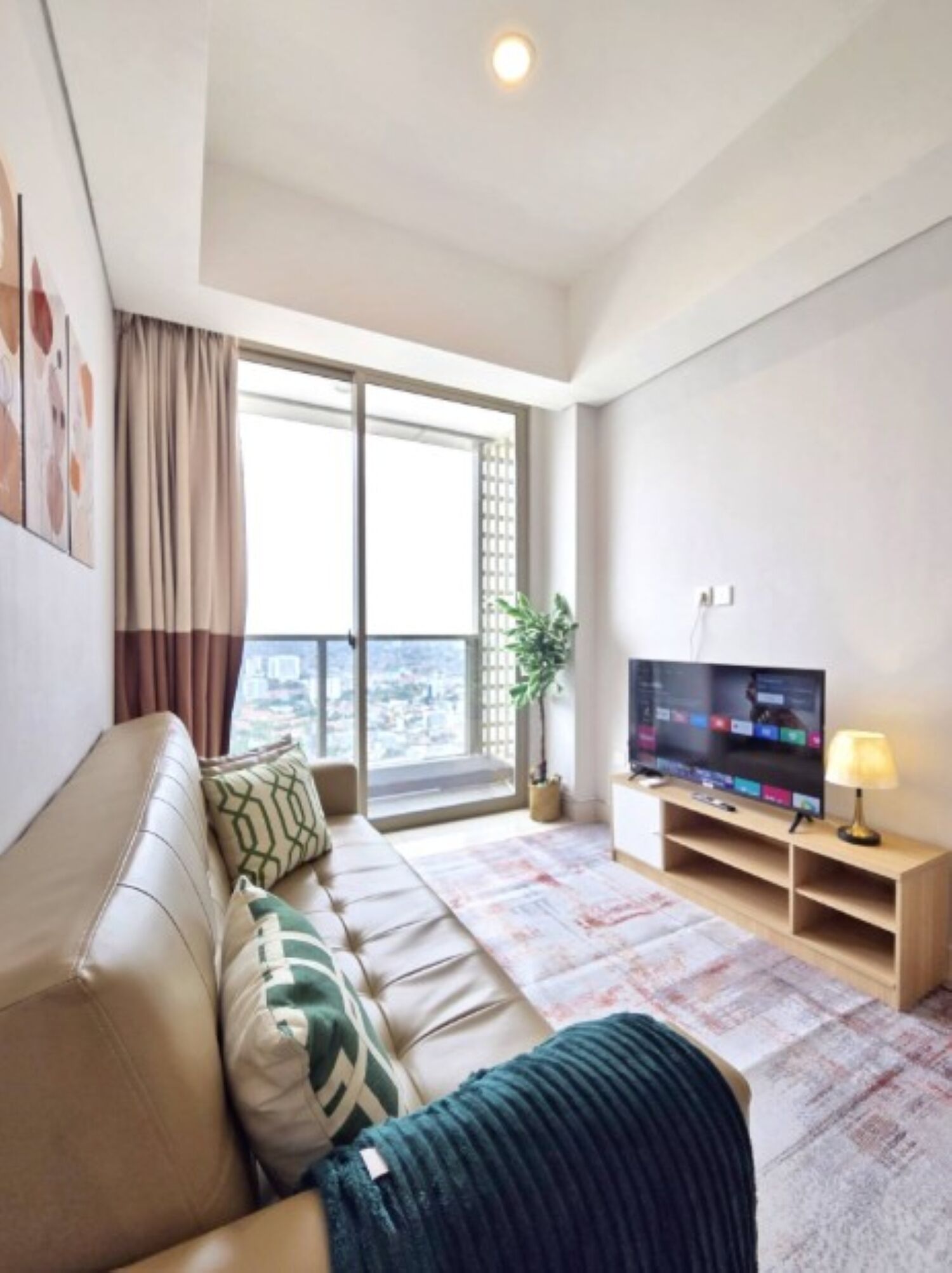 A modern living room with a sofa, television, and a view of the city through large windows.
