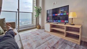 Una sala de estar con un ventanal grande, un televisor de pantalla plana, una planta y una lámpara.