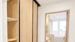 Un intérieur moderne avec une armoire en bois, une salle de bain dotée d’un lavabo et d’une douche, et une vue dégagée par une porte ouverte.