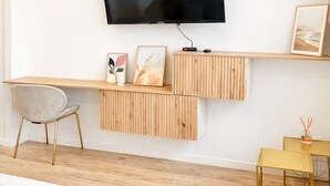 Un salon moderne avec un téléviseur à écran plat fixé au mur, des étagères en bois, un fauteuil à revêtement gris et un canapé à motifs rayés.