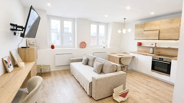 Un appartement moderne comprenant un canapé, une table à manger, une cuisine et un téléviseur fixé au mur.