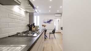 A modern kitchen with a gas stove, white brick backsplash, and a dining area with a chair. - Casa Valentina | WiFi Stazione Treni Parking (Modena)