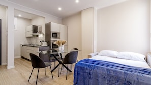 A compact hotel room with a bed, a small desk, and a kitchenette.