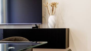 A modern living room with a flat-screen TV mounted on the wall, a black entertainment unit below, and a glass coffee table.