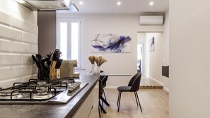 A modern kitchen with a gas stove, a coffee machine, and a dining area with a chair. - Casa Valentina | WiFi Stazione Treni Parking (Modena)