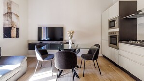 A modern kitchen with a flat-screen TV, a dining table with chairs, and a built-in oven. - House Chiara| WiFi Parking Station downtown Modena (Modena)