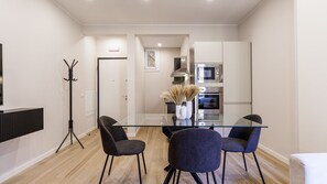 A modern kitchen with a glass dining table, four chairs, and stainless steel appliances.