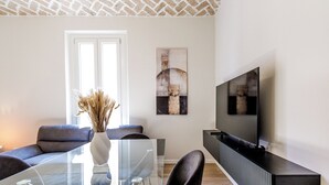 A modern living room with a glass dining table, grey sofas, and a flat-screen TV mounted on the wall. - House Chiara| WiFi Parking Station downtown Modena (Modena)