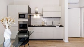 A modern kitchen with a gas stove, oven, microwave, and white cabinets. There is a dining table with chairs and a vase of dried flowers. - House Chiara| WiFi Parking Station downtown Modena (Modena)