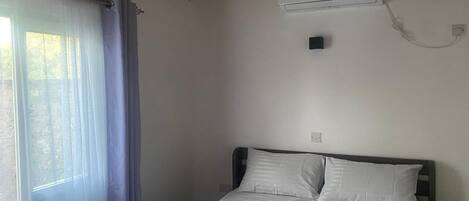A single bed with white bedding in a room with a wooden ceiling and an air conditioning unit mounted on the wall.