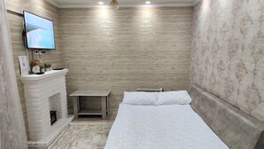 Une chambre à coucher avec un lit, un téléviseur fixé au mur, une cheminée et un papier peint à motifs.