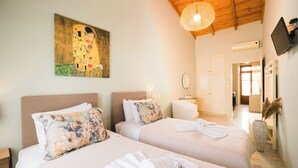 Ein Hotelzimmer mit zwei Betten, einem Bild an der Wand, einer Holzbalkendecke und einem an der Wand befestigten Fernseher.