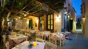 Ein Essbereich im Freien mit Tischen für zwei Personen, überdacht von einer mit Weinreben bewachsenen Pergola, und ein Schild, das ein Familienrestaurant kennzeichnet.
