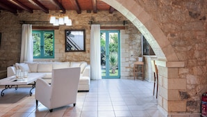 Un'ampia zona giorno con parete in pietra, soffitto in legno, divano bianco e tavolino da caffè.