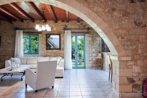 A spacious living area with a stone wall, a wooden ceiling, a white sofa, and a coffee table. - Villa Pinelopi - 350 meters away from sandy beach! (Rethymno)