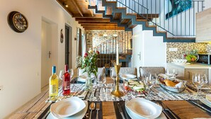 A dining area with a wooden table set for a meal, a staircase in the background, and a clock on the wall. - Beautiful sea views, Close to Beautiful Beaches of South Crete (Rethymno)