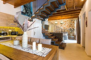 Une cuisine moderne avec un coin repas, un escalier menant à l’étage supérieur et un mur en pierre.