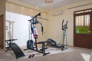 Ein Heimfitnessraum mit einer Hantelbank, einem Multifunktions-Trainingsgerät, einem Crosstrainer und Kurzhanteln.