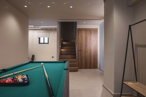 Ein Billardtisch mit Kugeln und Spielstangen, eine Treppe und eine Tür.