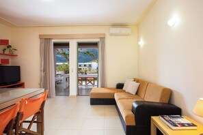 Ein modernes Hotelzimmer mit Sofa, Fernseher, Esstisch mit Stühlen und Blick ins Freie.