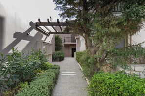 A narrow pathway leading to a building entrance, surrounded by dense greenery and a wooden pergola structure. - A & C Home 2: Two Bedroom Apartment 100m from Plakias Beach sandy beach (Rethymno)